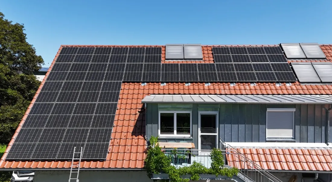 PV-Anlage auf einem Ziegeldach mit Balkon vor blauem Himmel